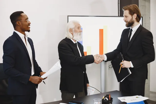 Three businessmen in suits having a meeting, shaking hands in front of a presentation chart. Appointment setting services: UK due diligence checklist