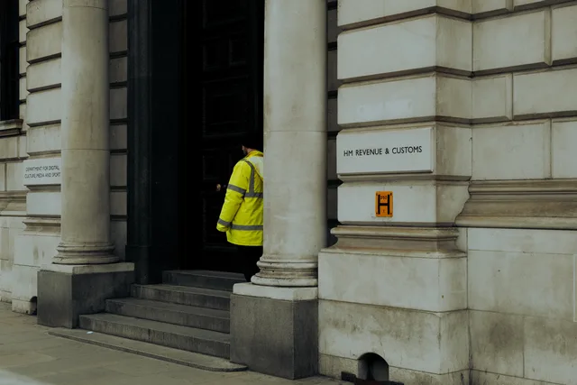 A guard in yellow jacket at the entrance of HM Revenue & Customs building in the UK. How IR35 changes contractor status at a UK appointment-setting agency