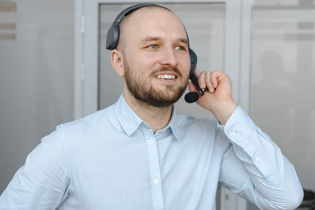 Smiling call center agent wearing a headset providing customer service in an office environment. SDR outsourcing: UK pay-for-performance risk and terms